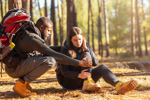 African-man-comforting-his-upset-caucasian-girlfriend,-woman-hurt-her-ancle-while-camping-in-forest,-free-space